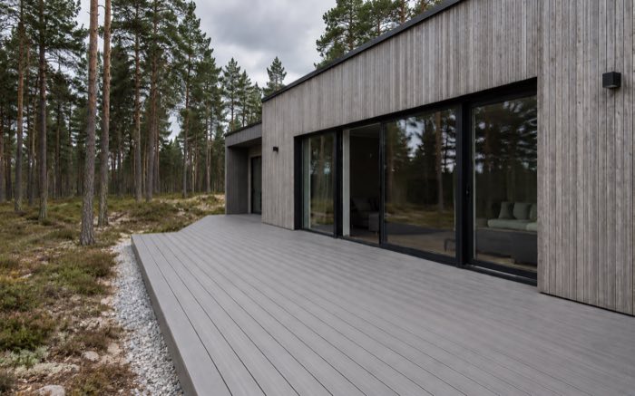 Harmaa komposiittiterassi modernin talon vieressä mäntymetsässä